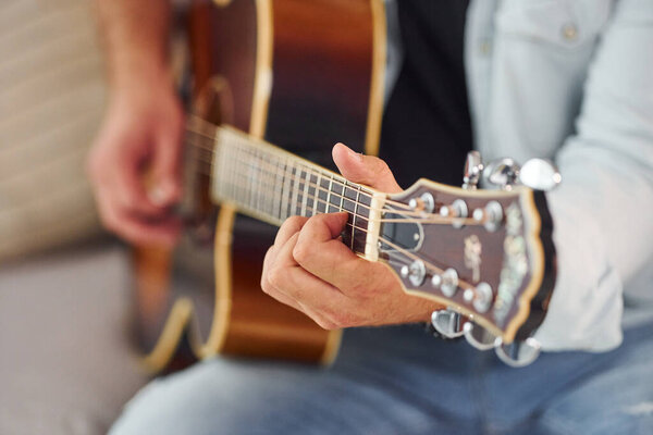 Close up view. Man in casual clothes and with acoustic guitar is indoors.