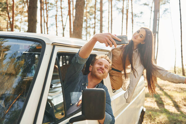 Making selfie. Young couple is traveling in the forest at daytime together.