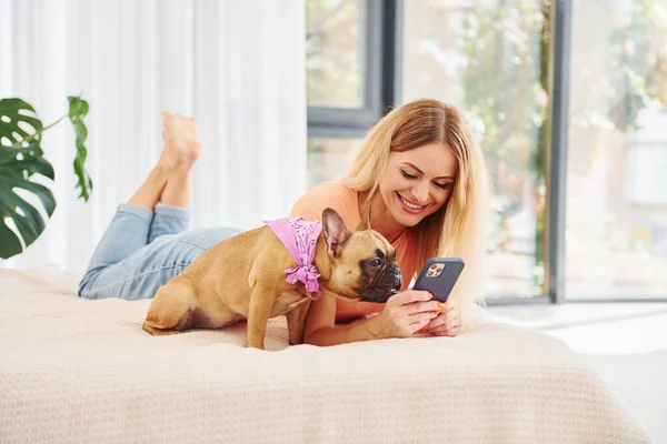 Holding phone. Woman with pug dog is at home at daytime.
