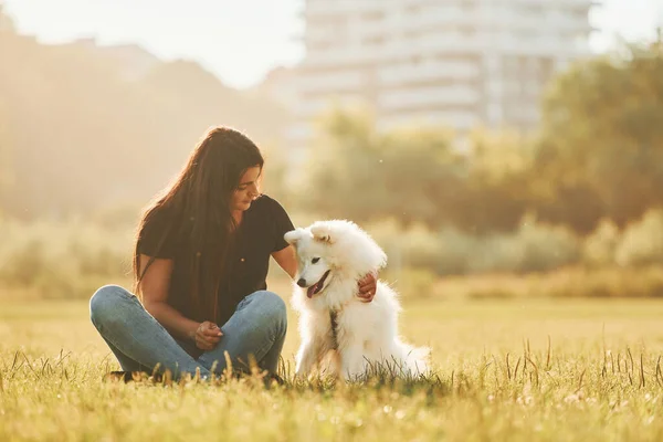 建物を背景に 彼女の犬と女性は晴れた日にフィールドで楽しんでいます — ストック写真