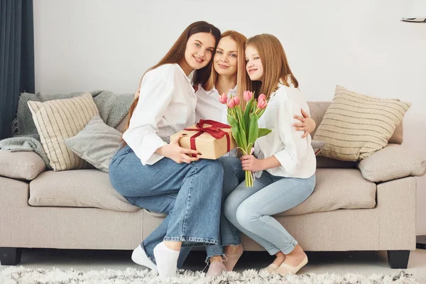 用鲜花让人惊讶年轻的母亲白天带着两个女儿在家里 — 图库照片