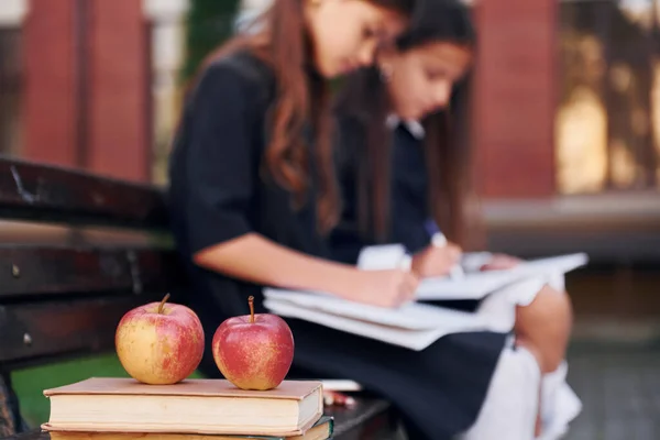 Books and apples. Two schoolgirls is outside together near school building.