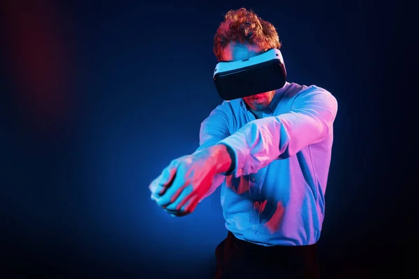 Virtual glasses gaming experience. Neon lighting. Young european man is in the dark studio.