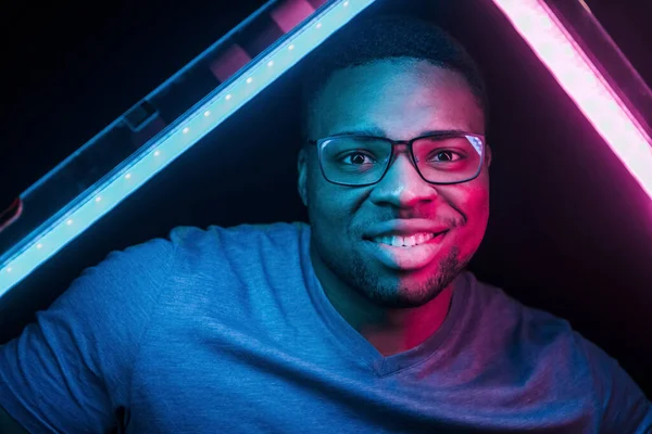 Holds lighting equipment. Futuristic neon lighting. Young african american man in the studio.