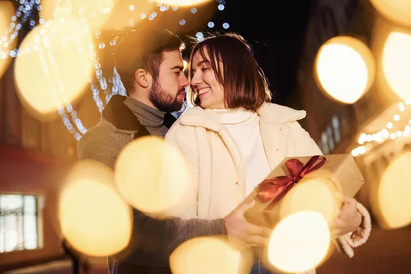 Kadının elinde hediye kutusu var. Mutlu genç çift sokakta yeni yılı kutluyor..