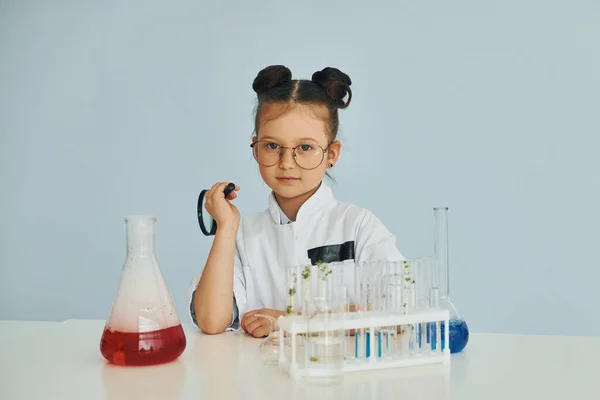 Works with test tubes. Little girl in coat playing a scientist in lab by using equipment.