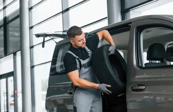 Mit Reifen Der Hand Mann Uniform Arbeitet Tagsüber Autosalon Stockfoto