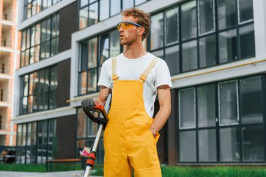 Dışarıda, avluda. Adam çimleri çim biçme makinesiyle kesiyor..