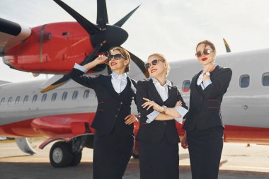 Üç hostes. Havaalanı ve uçak işçileri resmi giysiler içinde dışarıda birlikte duruyorlar..