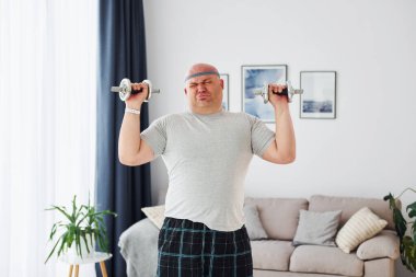 Dambıl kullanıyor. Sıradan giysili komik şişman adam evde..