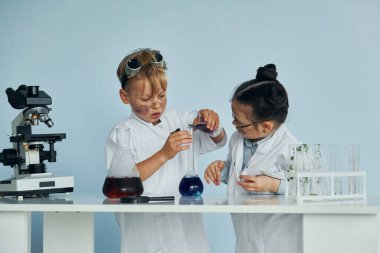 Beyaz önlüklü küçük kız ve oğlan laboratuarda ekipman kullanarak bilim adamlarıyla oynuyor..