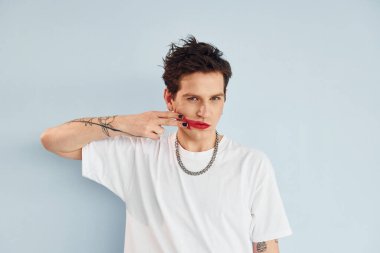 Genç eşcinsel adam stüdyoda duruyor ve kameraya poz veriyor. Dudaklar kırmızı rujla.