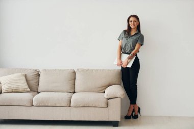 Kanepenin yanında beyaz duvara karşı duran resmi elbiseli bir kadın..