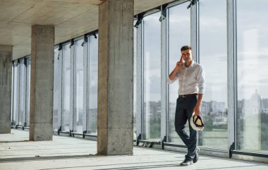 Yürüyor ve konuşuyor. Resmi kıyafetli genç adam içeride inşaatta çalışıyor..