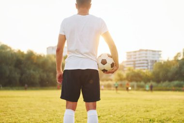 Ayakta duruyor ve topu elinde tutuyor. Genç futbolcu spor sahasında antrenman yapıyor..