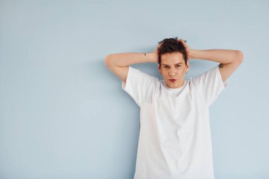 Genç eşcinsel adam stüdyoda duruyor ve kameraya poz veriyor. Sıradan beyaz gömlekli..