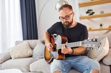 Enstrüman çalıyorum. Gündelik giysiler içinde ve akustik gitarlı bir adam içeride..