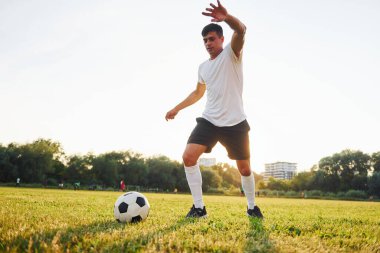 Aktif hafta sonu aktiviteleri. Arka planda orman var. Genç futbolcu spor sahasında antrenman yapıyor..