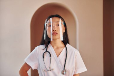 Koruyucu giysi içinde. Genç ciddi Asyalı kadın içeride duruyor..