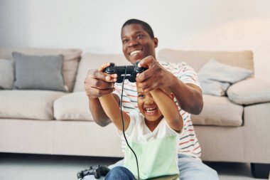 Elinde joysticklerle. Afrikalı Amerikalı baba ve küçük oğlu evde..