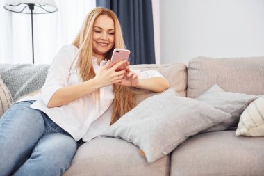 Kanepeye uzanmak. Beyaz gömlekli ve kot pantolonlu genç bayan evde..