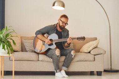 Şarkı yazma becerisi alıştırması yapıyorum. Gündelik giysiler içinde ve akustik gitarlı bir adam içeride..