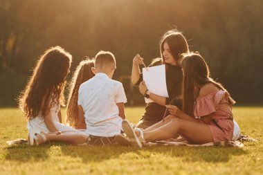 Kadın çizim yapmayı öğretiyor. Bir grup mutlu çocuk gündüz vakti spor sahasında..