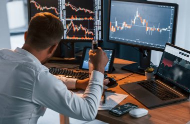 Alkolle. Resmi giyinmiş genç işadamı birden fazla ekranla ofiste..