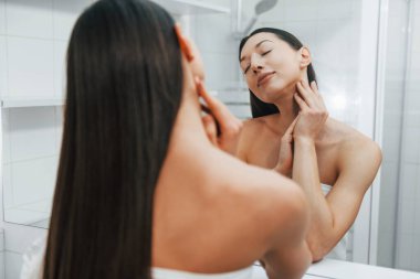 Cildine dikkat ediyor. İnce vücutlu beyaz kadın gündüz vakti evdedir..