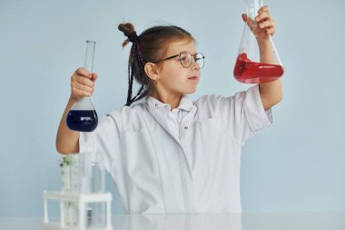 Palto giyen küçük bir kız laboratuarda ekipman kullanarak bilim adamını oynuyor..