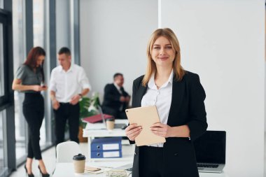 Meslektaşlarının önünde bir kadın. Ofiste resmi giysiler içinde bir grup insan var..
