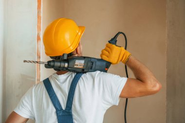 Alet kullanıyorum. Gündüz vakti inşaatta üniformalı genç bir adam çalışıyor..