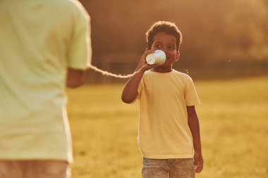 Düğümlü bardaklar kullanarak sohbet ediyorlar. İki Afrikalı Amerikalı çocuk yaz günlerinde tarlada birlikte eğleniyor..