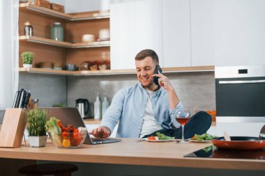 Telefonla konuşuyorum. Adam modern mutfakta evde yemek hazırlıyor..