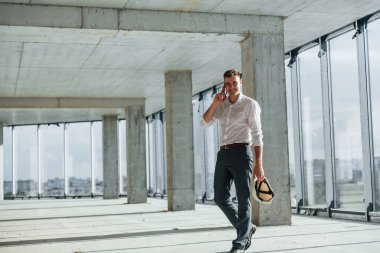 Yürüyor ve konuşuyor. Resmi kıyafetli genç adam içeride inşaatta çalışıyor..