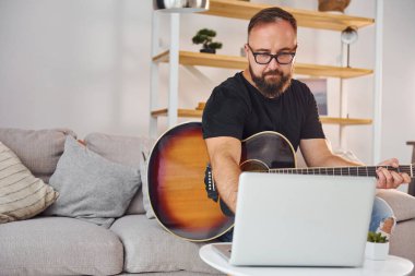 Laptop kullanıyorum. Gündelik giysiler içinde ve akustik gitarlı bir adam içeride..