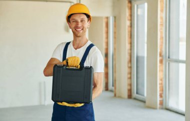 Kapalı bir odada, bitmemiş bir odada. Gündüz vakti inşaatta üniformalı genç bir adam çalışıyor..