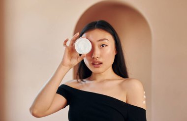 İçinde krema olan bir kap tutuyor. Genç ciddi Asyalı kadın içeride duruyor..