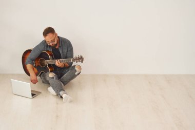 Dizüstü bilgisayarla. Gündelik giysiler içinde ve akustik gitarlı bir adam içeride..