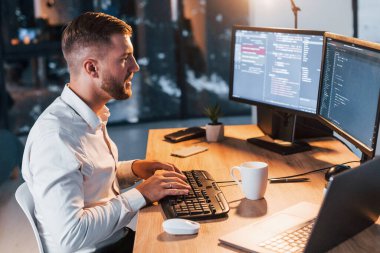 Ofiste bir kişi var. Resmi giyinmiş genç iş adamı birden fazla ekranda..