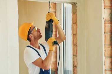 Talim bekletiliyor. Gündüz vakti inşaatta üniformalı genç bir adam çalışıyor..