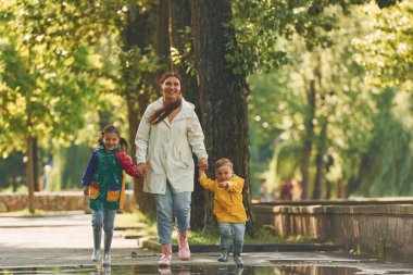 Ön manzara. Anne, küçük oğlu ve kızıyla yağmurdan sonra parkta yürüyüşe çıktı..