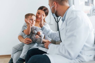 Küçük çocuk inceleniyor. Beyaz önlüklü iki doktor klinikte birlikte çalışıyorlar..