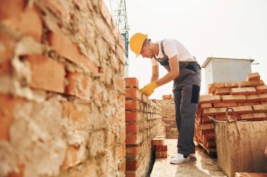 Tuğla kullanarak. Üniformalı genç inşaat işçisi tamamlanmamış binada meşgul..