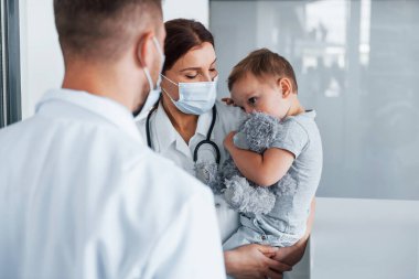 Küçük çocuk klinikte. Beyaz önlüklü iki doktor hastanede birlikte çalışıyorlar..