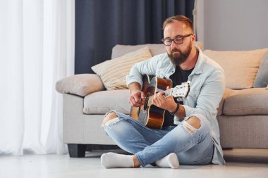 Yaratıcı uğraş. Gündelik giysiler içinde ve akustik gitarlı bir adam içeride..