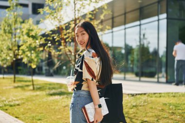 Öğrenci modern binanın yakınında yürüyor. Genç Asyalı kadın gündüz vakti dışarıda..