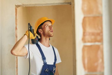 Alet kullanıyorum. Gündüz vakti inşaatta üniformalı genç bir adam çalışıyor..