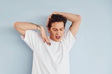 Genç eşcinsel adam stüdyoda duruyor ve kameraya poz veriyor..