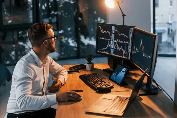 Akşamları çalışıyorum. Resmi giyinmiş genç işadamı birden fazla ekranla ofiste..